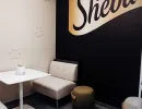 Kleiner Meetingraum mit Sheba-Logo, hellen Sitzmöbeln und Akzentwand in Schwarz-Gold