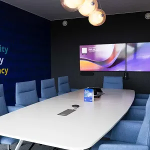 Konferenzraum mit blauen Sesseln, Werten an der Wand und Doppelbildschirm