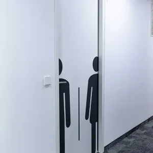 Tür mit stilisierten Symbolen für Damen und Herren im modernen Bürogang