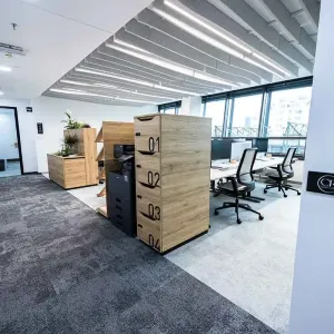 Blick entlang des Flurs mit Holzregalen, Drucker und hellen Arbeitszonen